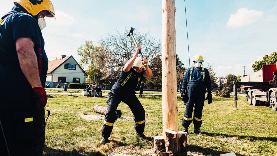 Firefighters using sledgehammers in an outdoor lumberjack demonstration with wooden pole.