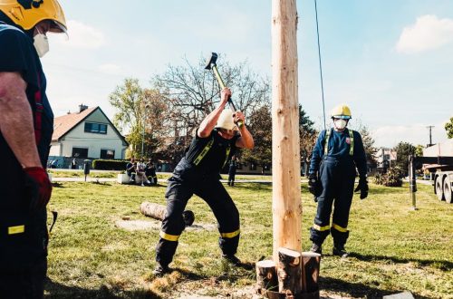 Firefighters using sledgehammers in an outdoor lumberjack demonstration with wooden pole.