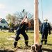 Firefighters using sledgehammers in an outdoor lumberjack demonstration with wooden pole.
